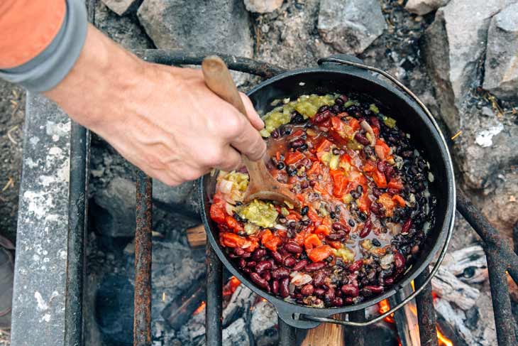 Cooking beans and vegetables in a Dutch oven over a campfire for vegetarian chili